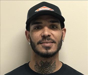 Headshot of half-smiling man wearing SERVPRO hat and uniform in front of gray background