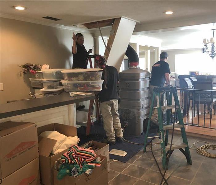 Three SERVPRO employees in a house performing a duct cleaning with gray machine connected through attic