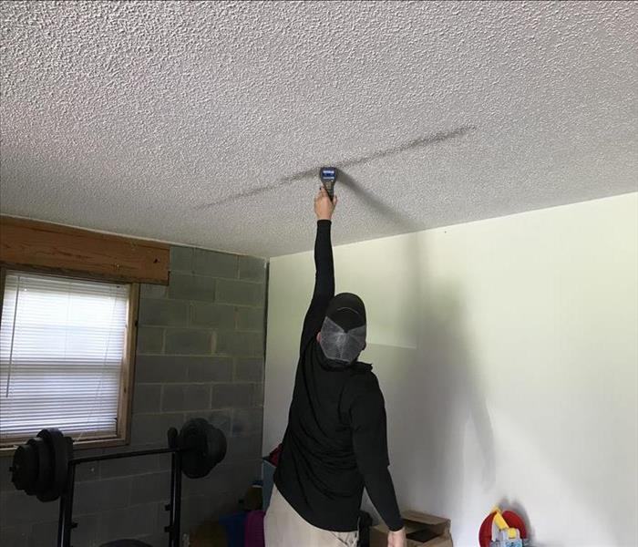 Male SERVPRO employee sticks device into dark spot on ceiling