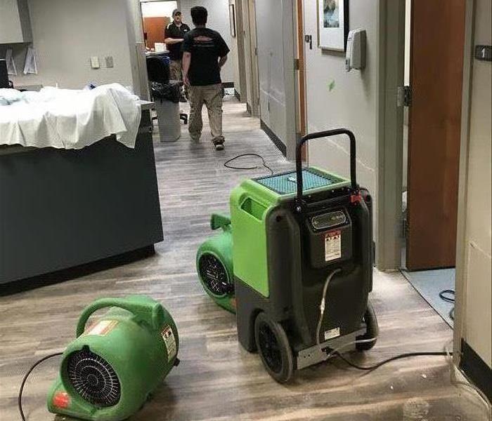 Employees walking down a hallway in a medical office with green machines in the foreground