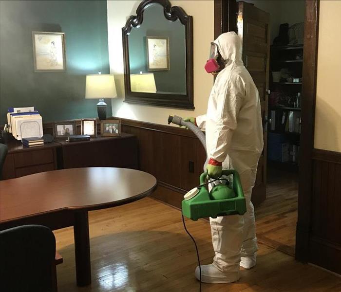 Person in white PPE directing a nozzle into a room