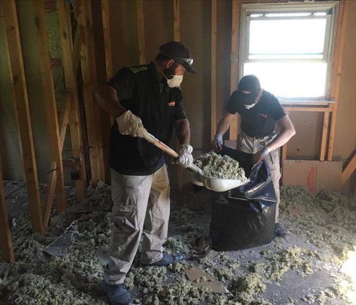 Two masked SERVPRO employees dumping debris into a bag