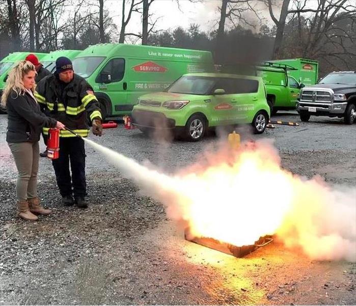 Firefighter directs woman using a fire extinguisher, both of whom are standing in front of SERVPRO vehicles