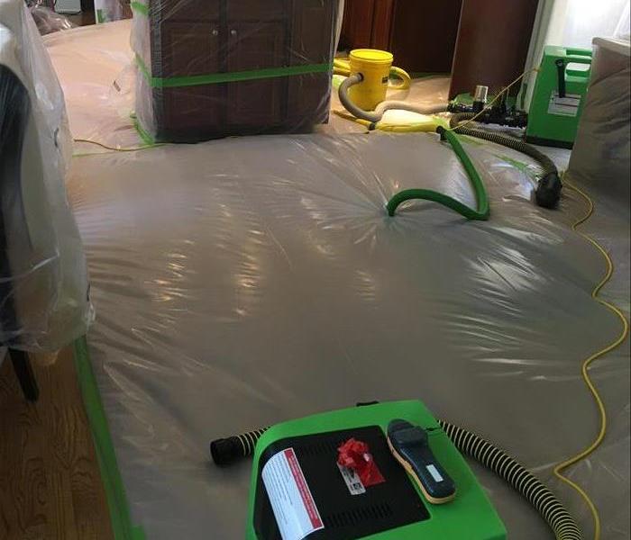 Green tubes and machines entering a plastic sheet on top of a hardwood floor