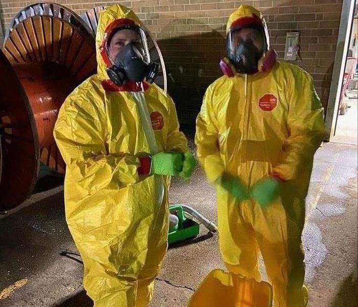 Two people in Tyvek suits standing in front of a brick wall