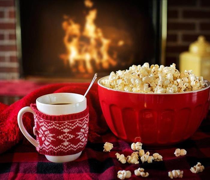 Red popcorn bowl and hot chocolate in front of a lit fireplace