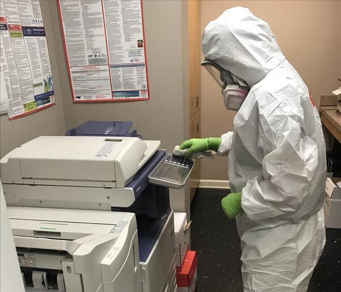 Person in white PPE spraying down office equipment